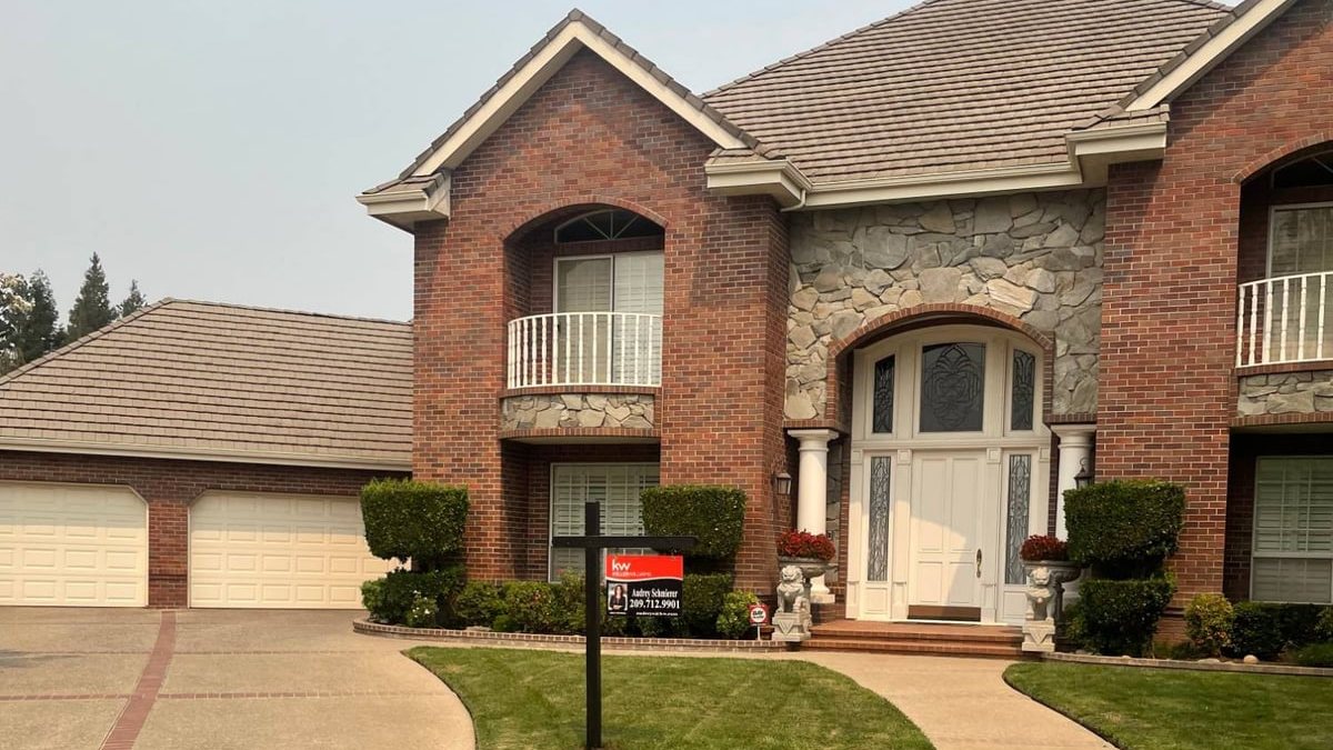 A two-story brick and stone home with a white front door and a Keller Williams yard sign showing Audrey Schmierer's name and phone number