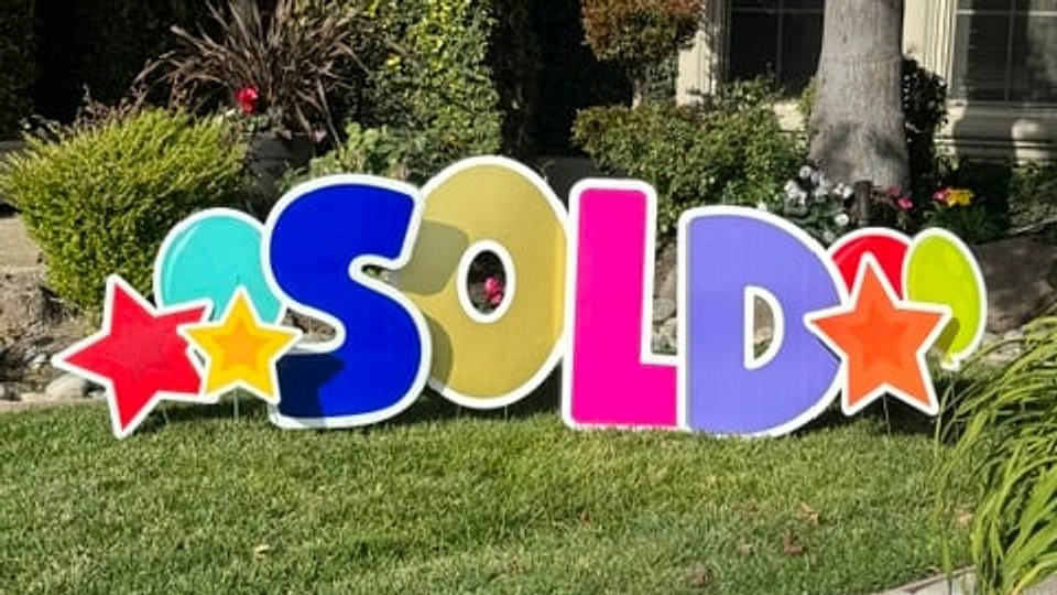 A colorful SOLD yard sign with stars on a green front lawn
